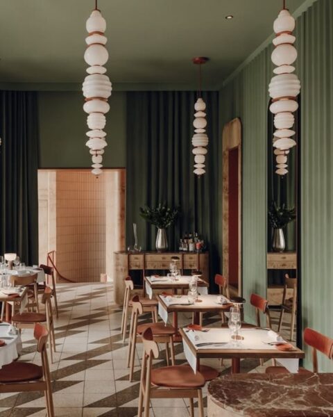 Restauracja Lupo w stylu art deco z zielonymi wnętrzami, koralowymi lampami i drewnianymi meblami. 