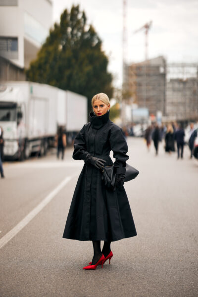 Elegancki look na ulicach Mediolanu; klasyczny czarny płaszcz z podkreślającymi styl czerwonymi butami na szpilce.