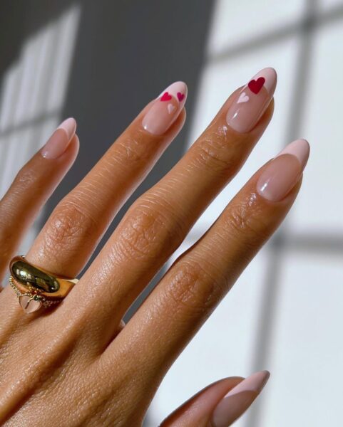 Stylowy manicure z przezroczystą bazą, ozdobiony minimalistycznymi różowymi i czerwonymi serduszkami na wybranych paznokciach. Migdałowy kształt paznokci dodaje elegancji.