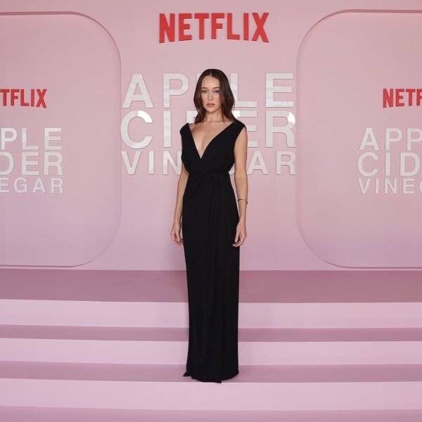 Milla Blake kto to: Alycia Debnam-Carey na premierze „Apple Cider Vinegar” – Aktorka Alycia Debnam-Carey w długiej, czarnej sukni z głębokim dekoltem pozuje na różowym tle z logotypem Netflixa. Jej elegancka stylizacja oraz delikatna biżuteria doskonale komponują się z oficjalnym charakterem wydarzenia.