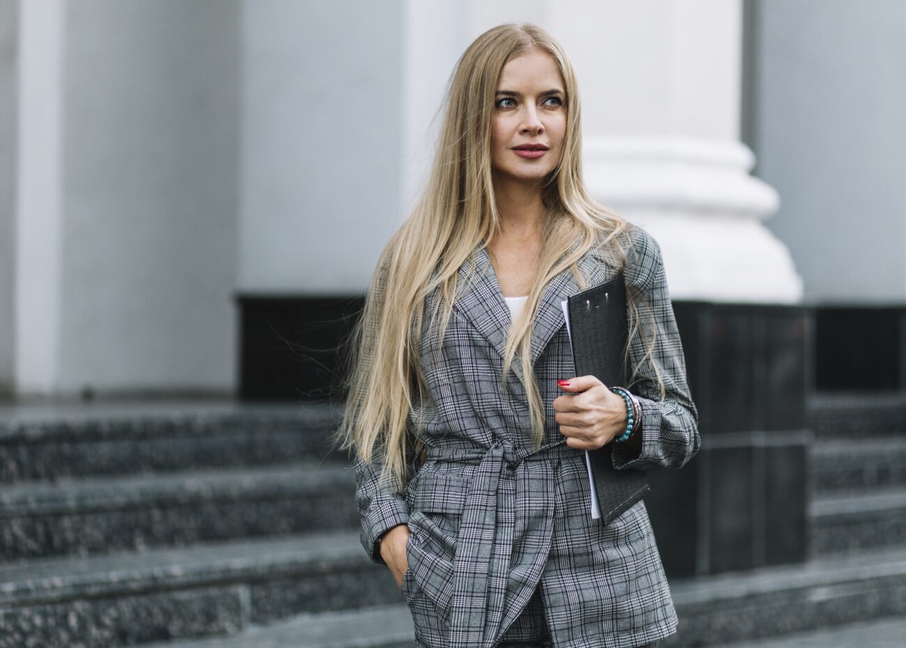 Garnitury damskie w miejskiej stylizacji. Blondynka nosi na sobie model w kratę przed schodami w mieście