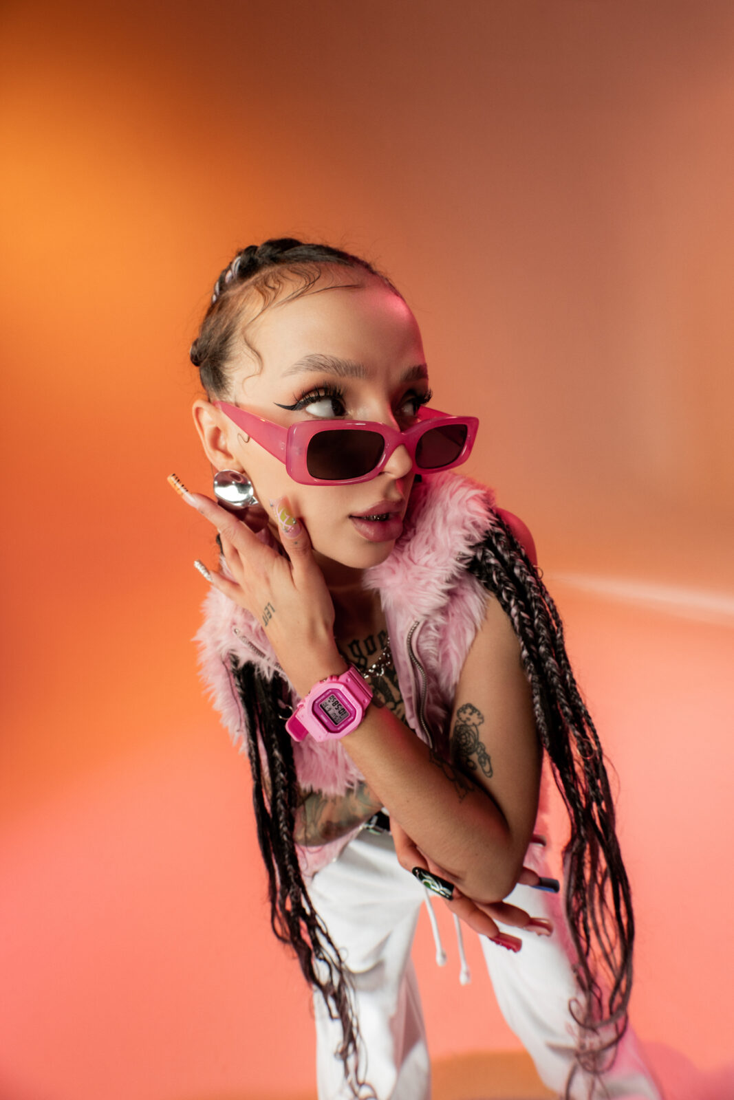 G-SHOCK: Power Pink Series Zbliżenie na twarz modelki w różowych okularach – Zdjęcie kobiety w okularach przeciwsłonecznych o mocnych, geometrycznych oprawkach, ubranej w różową futrzaną kamizelkę. Na ręku widoczny zegarek w neonowym odcieniu różu. Modelka prezentuje pewność siebie i ekstrawagancki styl.