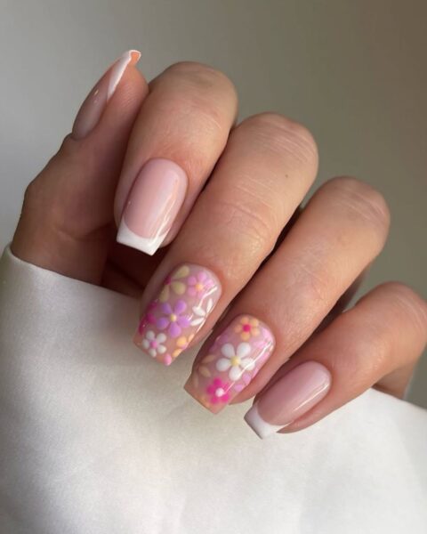 Zdjęcie ze zbliżeniem na dłoń z długimi, kwadratowymi paznokciami. Są pomalowane w stylu french manicure, a paznokcie palców wskazującego i serdecznego są ozdobione motywem malowanych kwiatów.