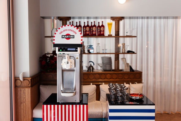Martini x Mateo Zielonka: Maszyna do lodów oznaczona napisem „Gelato Station Martini” ustawiona w restauracyjnym wnętrzu, obok metalowych pucharków i miseczek z dodatkami – przygotowana na letnie aperitivo.