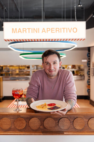 Kieliszki Martini Fiero i talerze z kolorowym ravioli w trzech wariantach – żółtym, czerwonym i fioletowym – serwowane z aksamitnym sosem na elegancko zastawionym stole.