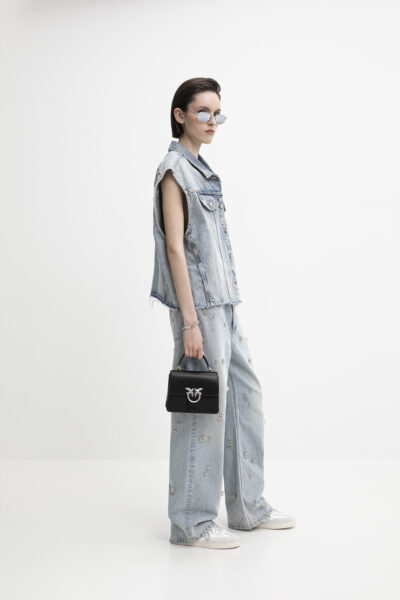 Denim total look w wersji dekonstrukcyjnej – bezrękawnik o surowych brzegach i szerokie spodnie z haftowanymi aplikacjami, uzupełnione sportowymi sneakersami i małą czarną torebką z metalicznym logo. Współczesna reinterpretacja stylu Y2K.