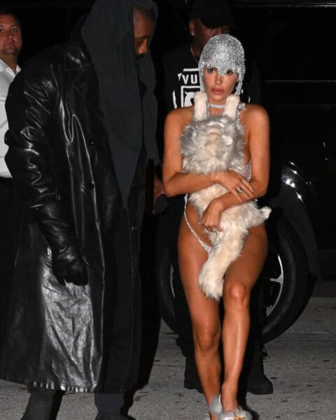 Bianca Censori i Kanye West podczas wysiadania z limuzyny. Kanye ma na sobie czarne spodnie, top, płaszcz skórzany i szalik na głowie. Za nim idzie Bianca Censori w bikini z futra, siatką na głowie i futerkowych szpilkach.