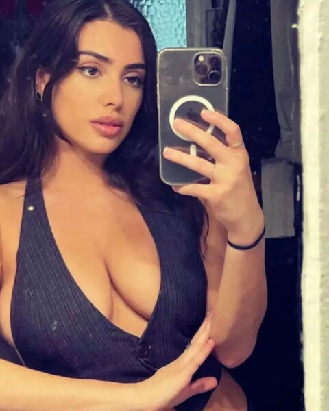 Zdjęcie celebrytki Bianci Censori, któa robi sobie selfie w lustrze. Ubrana jest w czarny top z głębokim dekoltem.