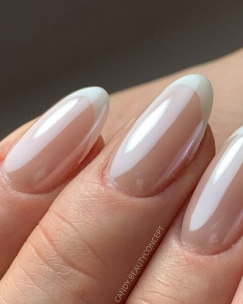 Zdjęcie dłoni ze zbliżeniem na długie, migdałowe paznokcie pomalowane w stylu french manicure z efektem glazed donut, czyli mocnym blaskiem.