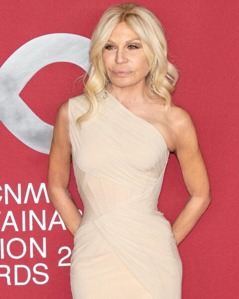 Donatella Versace z beżowej sukni na jedno ramię pozuje na ściance podczas eventu.