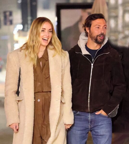 Zdjęcie Chiary Ferragni i Giovanni Tronchetti Provera wykonane przez paparazzi. Uśmiechnięta para idzie ulicą, trzymając się za ręce. Kobieta ma na sobie brązowy zestaw i beżowy płaszcz, a mężczyzna – jeansy, bluzę z kapturem i zamszową kurtkę.