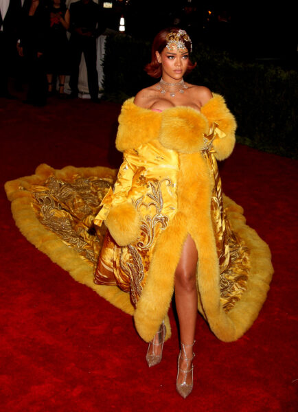 Rihanna zachwyca na czerwonym dywanie Met Gala 2015 w spektakularnej, haftowanej żółtej pelerynie projektu Guo Pei, wykończonej futrem i bogato zdobionym trenem, który przeszedł do historii jako jeden z najbardziej kultowych looków w historii wydarzenia.