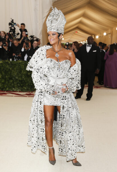 Rihanna pojawia się na Met Gala 2018 w olśniewającej srebrnej kreacji Maison Margiela inspirowanej papieską szatą, z wyszywanym ręcznie płaszczem, mini sukienką oraz imponującą tiarą – stylizacja nawiązuje do tematu „Heavenly Bodies: Fashion and the Catholic Imagination”.