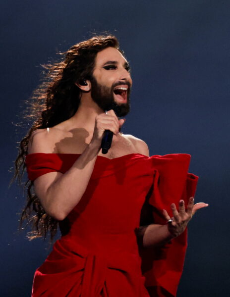 Conchita Wurst, zwyciężczyni Eurowizji 2014, śpiewa na scenie w spektakularnej czerwonej sukni z kokardą, stając się symbolem inkluzywności i odwagi sceny eurowizyjnej – jej występ i wizerunek przeszły do historii konkursu jako manifest różnorodności i siły.