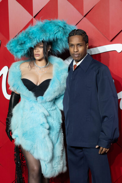 Rihanna w oszałamiającej błękitnej stylizacji z futra i kapelusza z piór, A$AP Rocky w granatowym garniturze – uchwycony moment, gdy para śmieje się wspólnie na czerwonym dywanie, prezentując silną więź i bezbłędny styl.
