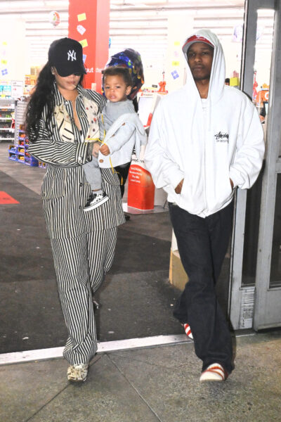 Rihanna w piżamowym komplecie w biało-czarne paski i czapce z daszkiem Yankees wychodzi ze sklepu z A$AP Rockym w sportowej bluzie Stüssy, trzymając ich wspólne dziecko – rodzinna chwila w luźnym, miejskim stylu.