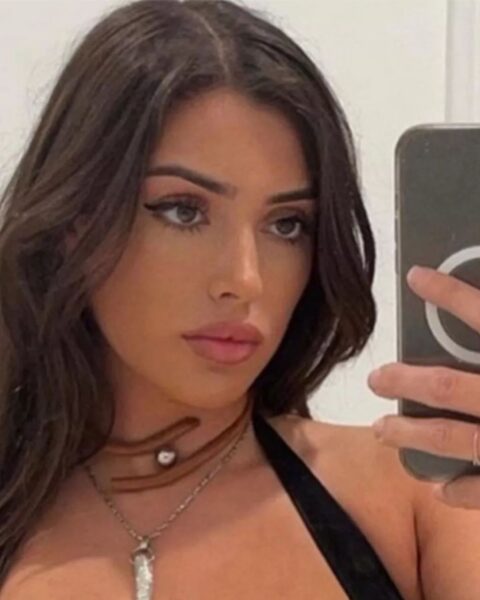 Bianca Censori przed Kanye Westem w długich, ciemnych włosach. Ma na sobie czarny top i kilka naszyjników. Robi sobie selfie telefonem.