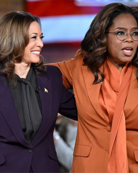 Zdjęcie Kamali Harris i Oprah Winfrey. Harris ma na sobie fioletowy garnitur i stoi ramię w ramię z Winfrey w pomarańczowym garniturze i bluzce. Występują obie w programie Winfrey.