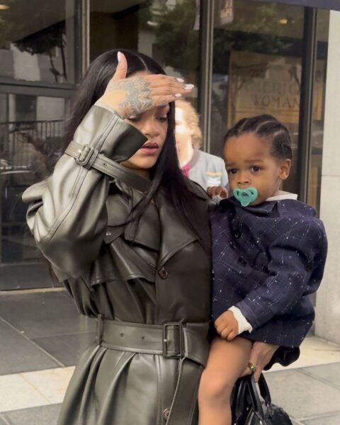 Rihanna i dzieci: na zdjęciu ma na rękach syna ubranego w granatową kurtkę. Sama ubrana jest w skórzany, oliwkowy płaszcz. Ma rozpuszczone włosy. Zasłania twarz dłonią przed zdjęciami.