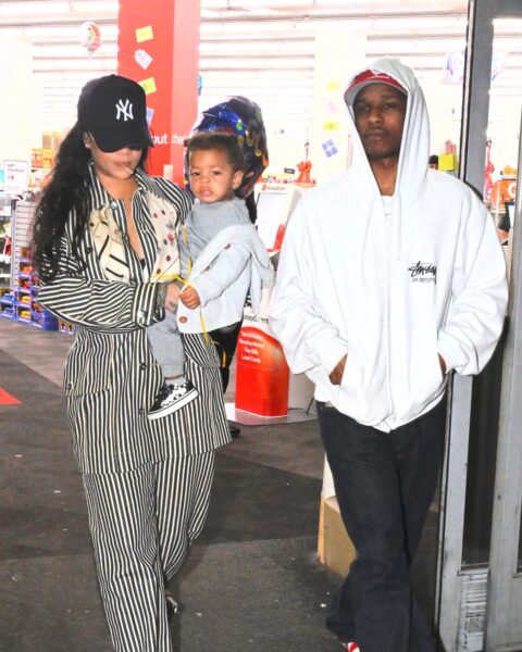 Rihanna i jej partner ASAP Rocky. Rihanna jest ubrana w garnitur w czarno-białe prążki i czapkę z daszkiem. Nosi na rękach syna w szarym dresie i szarej bluzie. Obok idzie ASAP Rocky w białej bluzie, czapce z daszkiem i czarnych spodniach dresowych. Idą przez parking.