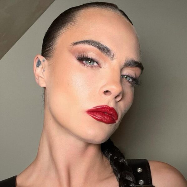 Cara Delevingne w mocnym makijażu z czerwonymi ustami i mocno podkreślonymi brwiami. Ich kształt pasuje do jej twarzy.