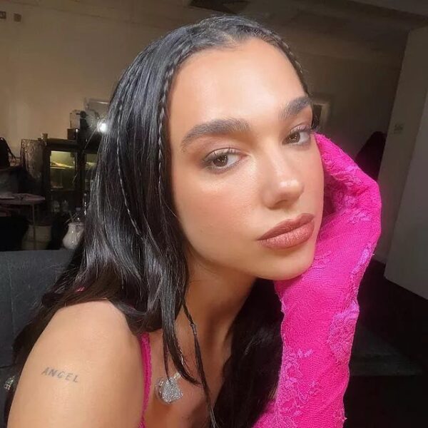 Dua Lipa w letniej fryzurze typu baby braids. Piosenkarka pozuje przed koncertem w różowych rękawiczkach z koronki.