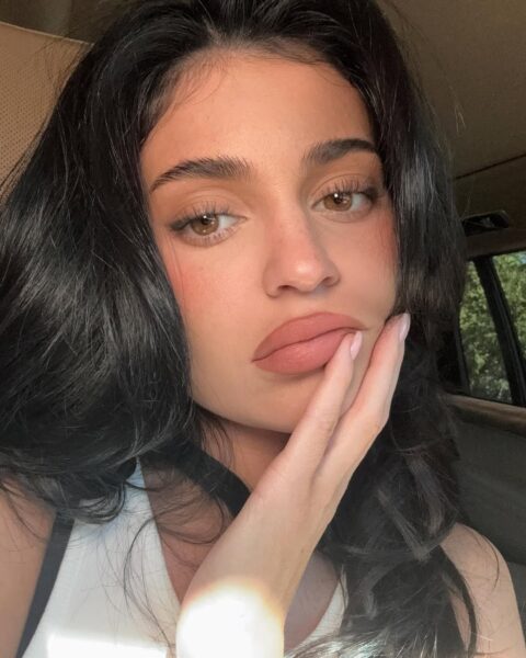 Kylie Jenner z naturalnym kształtem brwi, który pasuje do jej twarzy. Celebrytka ma rozpuszczone włosy, pozuje w białym topie.