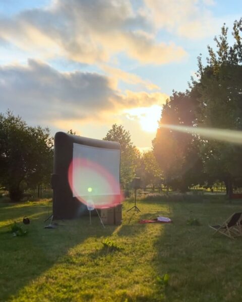 Zdjęcie przedstawiające kino plenerowe na polanie. Widać wielki ekran do wyświetlania filmów. 