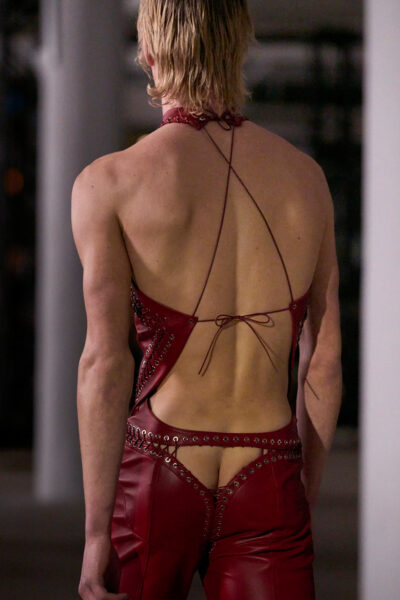 Model w bordowym zestawie ze skóry z wycięciami na pośladkach i plecach, ze sznurowanym topem w stylu bondage. Look z pokazu Ludovica de Saint Sernina na sezon Jesień/Zima 2024 ukazuje granicę między modą a performansem.