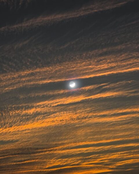 Zdjęcie nocnego nieba z chmurami, zza których widać pełnię Księżyca.