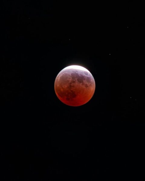 Zdjęcie nocnego nieba z Księżycem w pełni, który opalizuje na czerwono-pomarańczowo.