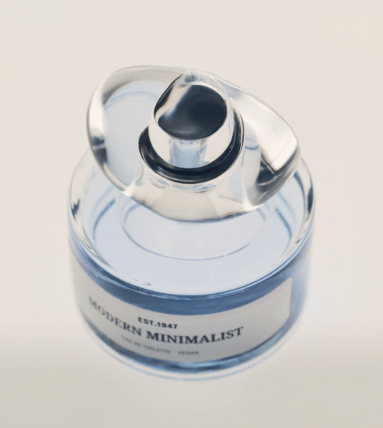 Perfumy „Modern Minimalist” w butelce wypełnionej niebieskawym płynem, ukazane z góry. Charakterystyczny korek z przezroczystego szkła oraz nowoczesna, prosta etykieta podkreślają czystość i estetykę minimalistycznego designu.